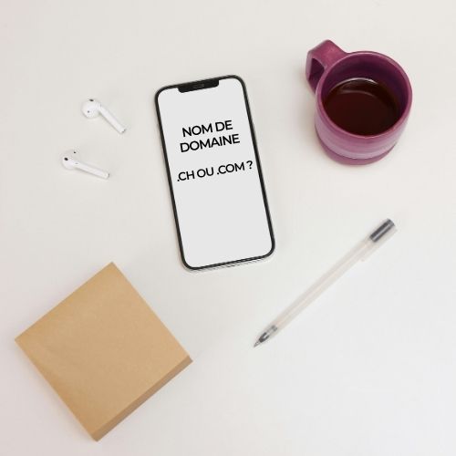 Téléphone affichant "Nom de domaine, .com ou .ch ?" posé sur une table avec un carnet, un café et un stylo