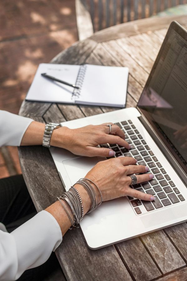 Mains avec bijoux tapant sur un clavier d'ordinateur, posé sur une table en bois, ambiance travail en extérieur