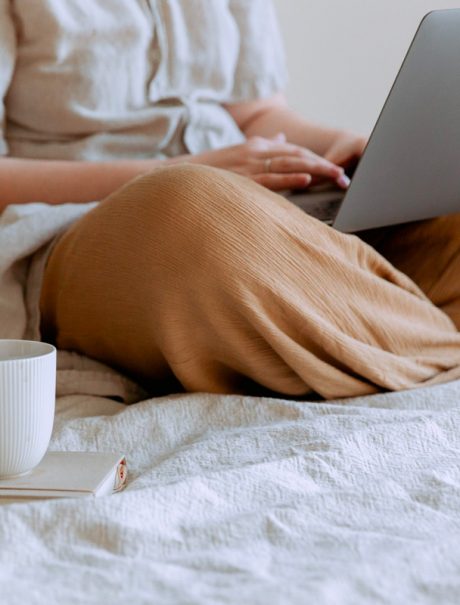 femme assise en tailleur sur un lit avec un tasse de thé et un macbook